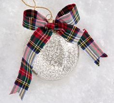 a glass ornament with a red, white and green plaid bow on it