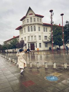 a woman walking down the street in front of a large white building on a rainy day