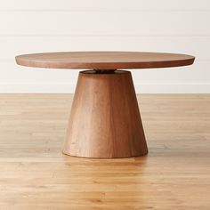 a round wooden table on a hard wood floor with white walls in the backround