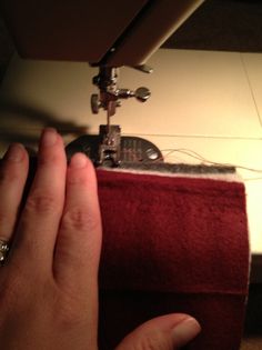 someone using a sewing machine to sew something on a piece of red material that is sitting on the floor