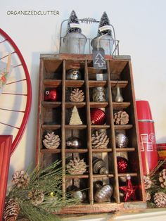 an old wooden box filled with ornaments and pine cones on top of a mantle next to a fan