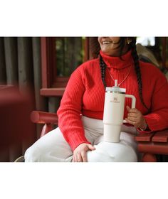 a woman sitting on a red bench holding a white cup and smiling at the camera