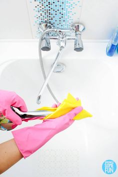 a person in pink gloves is cleaning a white bathtub with yellow and blue sponges