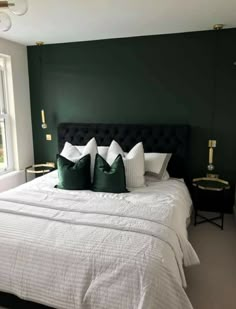 a bedroom with green walls and white bedding, black headboard and two pillows