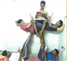 four people sitting on top of each other in a room with one person holding a book