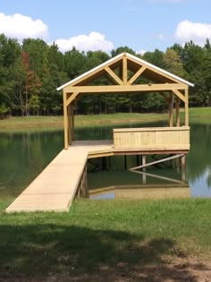 a wooden dock sitting on top of a lake next to a lush green field and forest