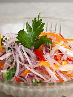 a salad in a glass bowl with carrots, onions and parsley on top