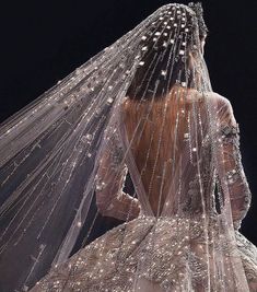 the back of a woman's wedding dress with long veil and sparkling beads on it