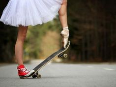 a girl in a tutu and red tennis shoes is riding her skateboard down the street