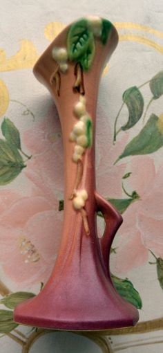 a pink vase sitting on top of a table next to a flowery wallpaper