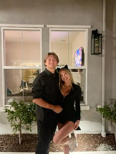 a man and woman posing for a photo in front of a house with their arms around each other