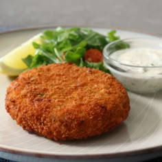 a plate with some food on it next to a bowl of dip and lemon wedges