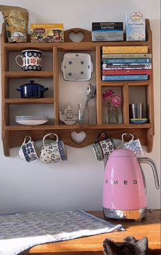 a wooden shelf filled with lots of books and tea cups next to a pink kettle