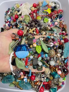 a person's hand holding a container filled with lots of different types of jewelry