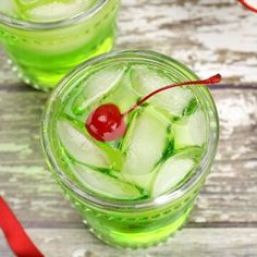 two glasses filled with ice and cherries next to a red ribbon on a wooden table