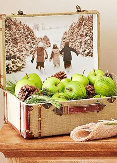 an open suitcase filled with green apples on top of a wooden table next to a christmas tree