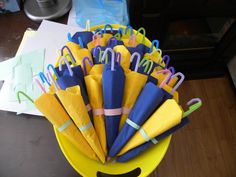 there are many different colored umbrellas in the yellow bucket on the table with papers