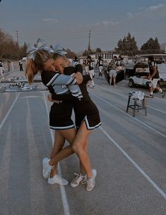 two girls in cheer uniforms hugging each other on the side of a road with people behind them