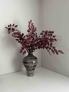 a vase filled with red flowers sitting on top of a white table next to a wall