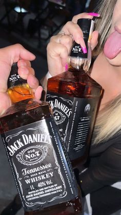 a woman sticking her tongue out and holding two bottles of jack daniels whiskey in front of her face