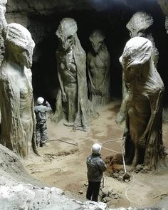 a group of statues in a cave with one man standing next to the other and looking at something