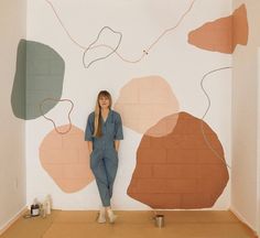 a woman is standing in front of a wall with abstract shapes painted on the walls