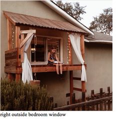 a woman sitting on the ledge of a porch with curtains hanging from it's windows