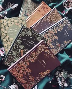 four different colored books laying on top of a blue cloth covered tablecloth with floral designs