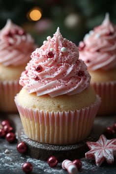 three cupcakes with pink frosting and sprinkles on a table