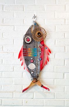 a fish hanging on a brick wall next to a wire and wood hook with an eyeball in it