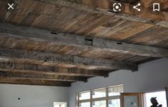 a woman standing in front of a window next to a wooden ceiling with exposed beams