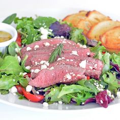 a white plate topped with meat and salad next to bread on top of a table