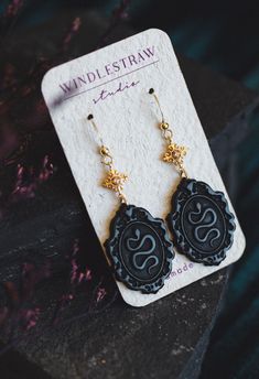 two black and gold earrings sitting on top of a piece of paper