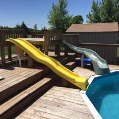 a yellow slide sitting on top of a wooden deck next to a swimming pool in a backyard