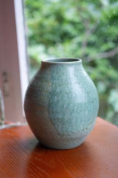 a green vase sitting on top of a wooden table next to a window sill