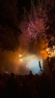 fireworks are lit up in the night sky as people watch from their seats at an outdoor concert