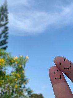 two fingers with faces drawn on them in front of some trees and blue skys