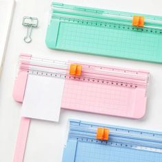 three different colored rulers with orange clips attached to them on a white surface next to a clipboard