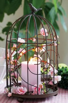 a candle in a birdcage with pink flowers