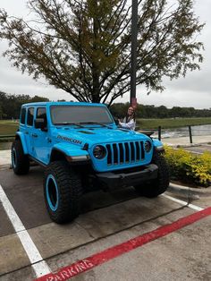 a bright blue jeep parked in a parking lot next to a tree and shrubbery