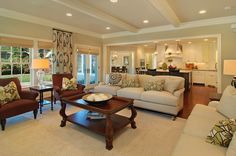 a living room with couches, chairs and tables in front of a kitchen area