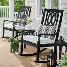 two black rocking chairs sitting on top of a porch next to a plant and lantern