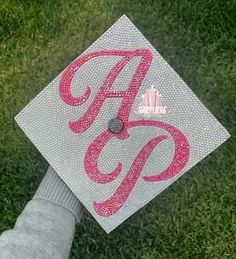 a person's hand holding a graduation cap with the letter a in pink on it