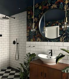 a bathroom with black and white tiled walls, a round mirror above the sink, and a checkered floor