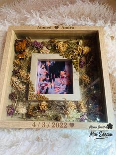 a photo frame with flowers and leaves in it sitting on a fluffy white blanket next to a teddy bear