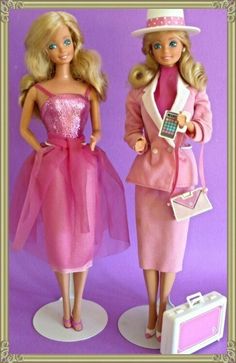 two barbie dolls standing next to each other in front of a purple background with a suitcase