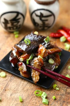 some food is on a black plate with chopsticks