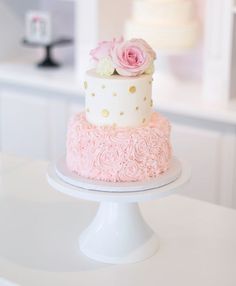 two tiered cake with pink and white frosting roses on the top, sitting on a pedestal