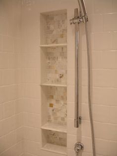 the shower head is open and there are shelves in the shower stall that have tiles on them