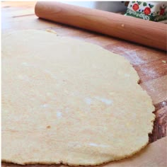 an uncooked pizza dough sitting on top of a wooden table next to a rolling pin